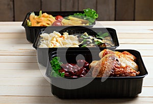 Ready meals to eat, containers with fried chicken wings and raw vegetables on rustic background, cherry tomato  and micro greenss