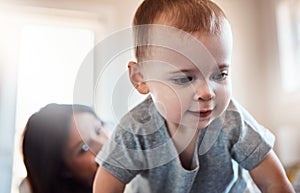 Ready or not, here I come. an adorable baby girl crawling on a bed with her mother in the background.