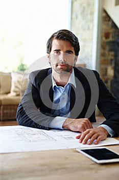 Ready for presenting to the client. A young architect sitting at his desk with his floor plans spread out in front of