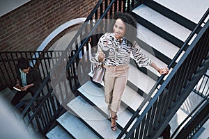 Ready, set, go get that success. a confident young businesswoman walking up the stairs in a modern workplace.