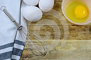 Ready to bake with eggs and a wisk on a wooden background.