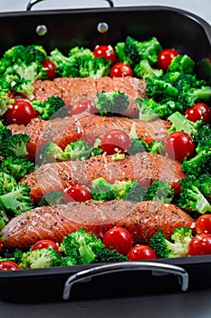 Ready to bake raw salmon fillet with broccoli and tomato on frying tray, vertical closeup