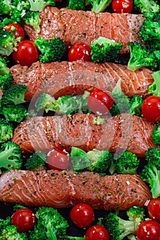 Ready to bake raw salmon fillet with broccoli and tomato on frying tray, vertical, top view, closeup