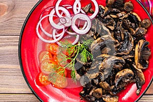 Ready-to-eat appetizer - fried mushrooms, cherry tomatoes and onions on a plate on a wooden table