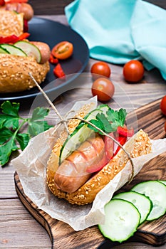 Ready-to-eat appetizing hot dog made from fried sausage, rolls and fresh vegetables, wrapped in parchment paper on a cutting board