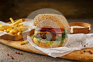 Ready-to-eat delicious hamburger and hot French fries. A cutting board made of mango wood in a rustic style. Fresh herbs and