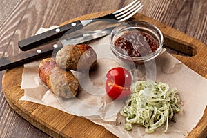 Ready-to-eat pigs sausages wrapped in bacon on wooden board. Fried savory sausages wrapped in bacon served with onion