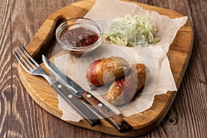 Ready-to-eat pigs sausages wrapped in bacon on wooden board. Fried savory sausages wrapped in bacon served with onion