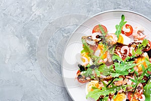 Ready-to-eat salad with cherry tomatoes, eggs, boiled shrimp, arugula, sesame seeds and balsamic sauce in a plate on the table