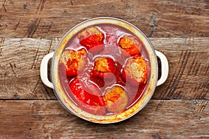 Ready to eat sweet peppers stuffed with meat and rice with sauce in a saucepan on a wooden background, top view