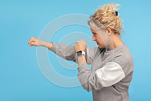 Ready to fight! Side view of feisty woman with short curly hair in sweatshirt punching to side with aggressive expression photo