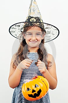 Ready to go trick-or-treating. a little girl wearing a witch hat while holding a jack o lantern against a white