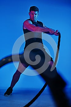 Ready to knock those obstacles out. Blue filtered shot of a man working out with battle ropes in the studio.