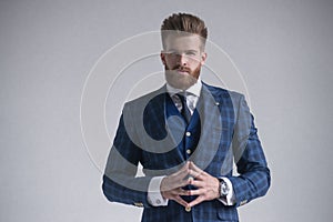 Ready to negotiate. Thoughtful young businessman holding hands clasped and looking at camera while standing against grey photo