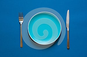 Color plate fork and knife isolated on blue background.
