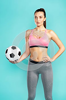 Ready to play. Young sporty woman in sportswear holding soccer ball while standing against blue background