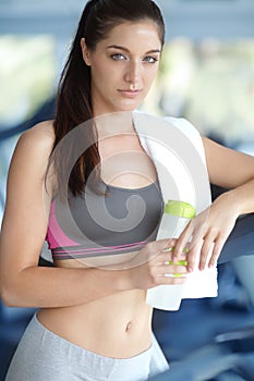 Ready to take on the treadmill. A beautiful young woman leaning on a treadmill holding a water bottle at the gym.