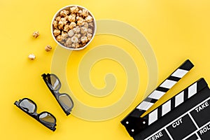 Ready to watch film. Clapperboard, glasses and popcorn on yellow background top view copyspace