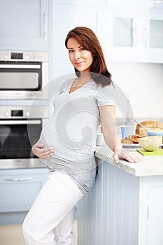 Ready and waiting. Portrait of a beautiful pregnant woman standing in the kitchen holding her stomach.