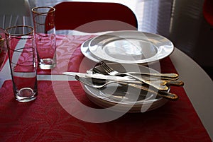 Ready white plates, forks, knives and glasses on the table. Crockery and cutlery on a red tablecloth.
