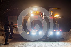 Truck traffic accident at night, on a snowy winter road. Strongly illuminated Wrecker truck pulls a truck out of snow hanging.