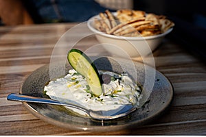 Real authentic photo of fresh Greek Tzatziki yogurt dip and pita bread and pickels in restaurant under golden hour