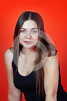 Real beautiful woman with dark hair, blue eyes and plump cheeks, in black underwear, sitting on bright red background.