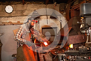 Real brutal blacksmith works in a workshop with a red-hot iron.