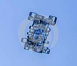 Real culomn snowflake at high magnification. Macro photo of small rimmed snow crystal, snowflake glowing on dark blue