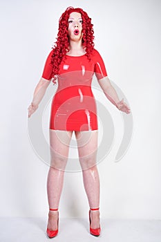 Real doll woman wearing red latex rubber dress and posing on white studio background alone. curvy plus size adult girl standing as