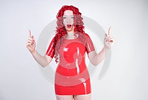 Real doll woman wearing red latex rubber dress and posing on white studio background alone. curvy plus size adult girl standing as