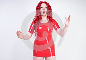 Real doll woman wearing red latex rubber dress and posing on white studio background alone. curvy plus size adult girl standing as