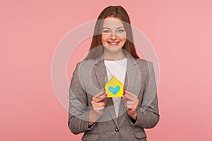 Real estate agency. Portrait of elegant positive woman in business suit holding paper house with heart inside