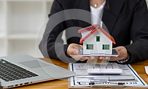 Real estate agent advising clients with contract documents and computers with front view house designs.