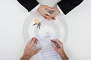 Real Estate Agent With Customer Signing Contract At Desk