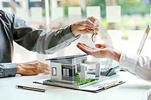 The real estate agent gives the buyer the house keys on a table with modern miniature house model