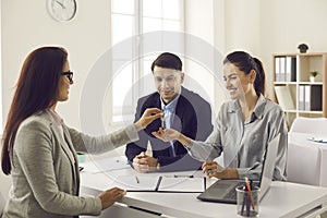 Real estate agent gives the keys to her new home to a married couple at a meeting in the office.