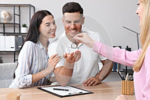 Real estate agent giving house key to couple at table in office