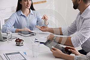 Real estate agent giving house key to young couple in office, closeup. Mortgage concept