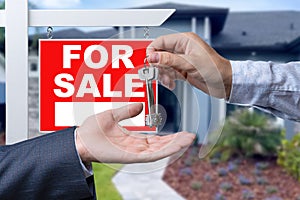 Real Estate Agent Handing Over the House Keys in Front of a Beautiful New Home and For Sale Real Estate Sign.