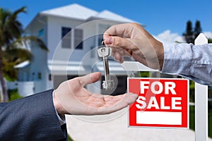 Real Estate Agent Handing Over the House Keys in Front of a Beautiful New Home and For Sale Real Estate Sign.