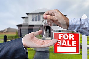 Real Estate Agent Handing Over the House Keys in Front of a Beautiful New Home and For Sale Real Estate Sign.