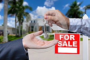 Real Estate Agent Handing Over the House Keys in Front of a Beautiful New Home and For Sale Real Estate Sign.