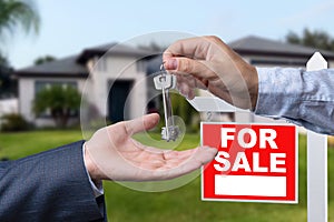 Real Estate Agent Handing Over the House Keys in Front of a Beautiful New Home and For Sale Real Estate Sign.