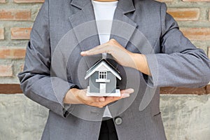 Real estate agent hands holding the home model stand in front of the red brick wall background or Sales presenting home insurance