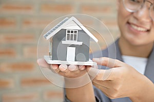 Real estate agent hands holding the home model stand in front of the red brick wall or Sales presenting home insurance
