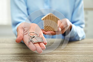 Real estate agent holding house figure and key at table, closeup