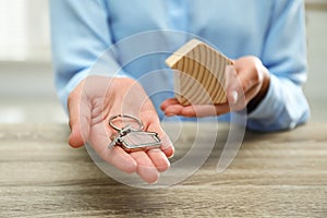 Real estate agent holding house figure and key at table, closeup