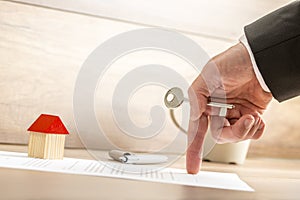 Real estate agent holding house key while showing with his finger where to sign a contract of house sale