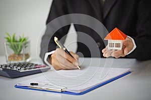 Real estate agent holding house model,  customer signing contract to buy house, insurance or loan real estate